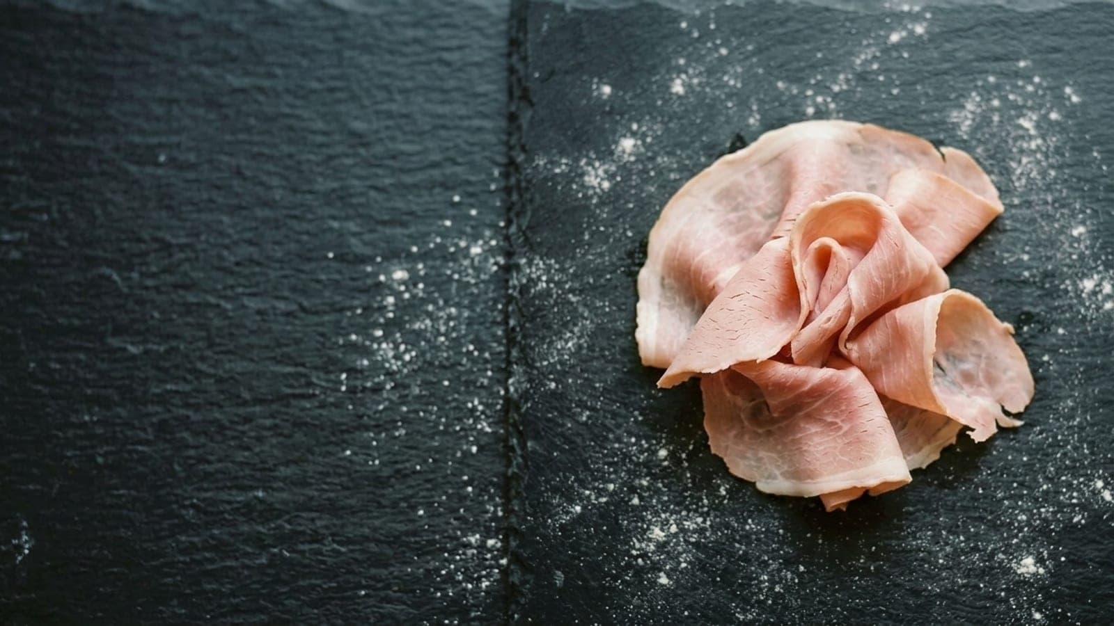 Thin slices of pale rosy prosciutto cotto torn into ribbons on dark slate