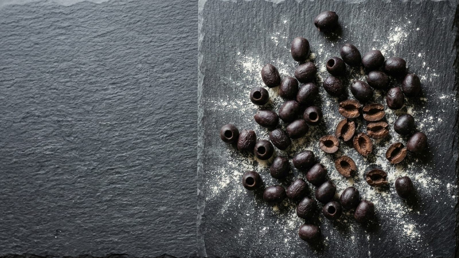 Pitted black olives, whole and halved, scattered on dark slate