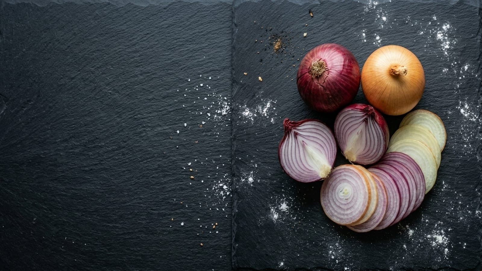 A red onion and a yellow onion, one halved, with thin slices fanned out beside them on dark slate