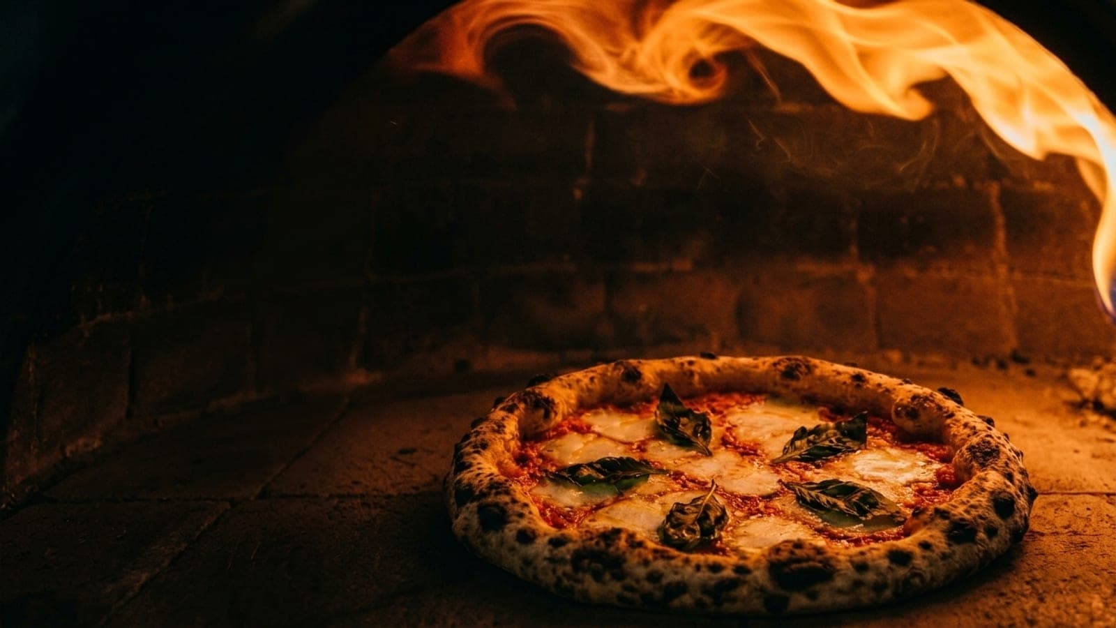 A Neapolitan pizza baking in a wood-fired outdoor oven, flames curling around it.