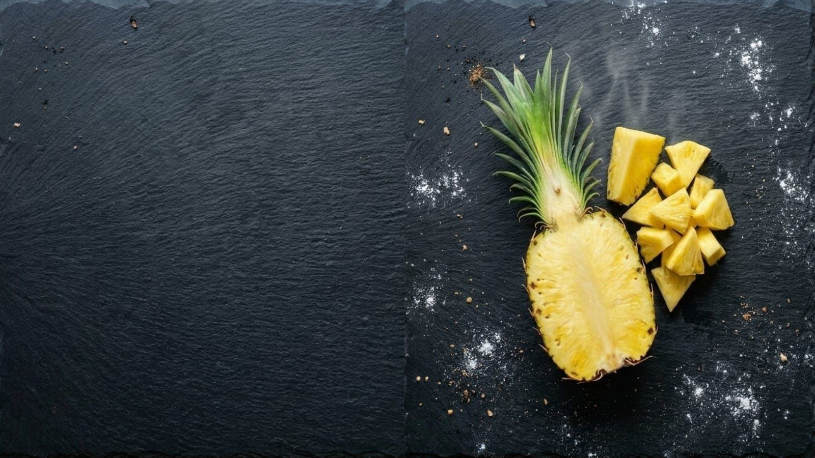 A halved fresh pineapple beside a small pile of golden, well-drained pineapple tidbits on dark slate