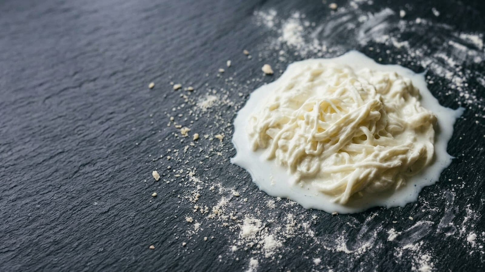 A soft loose mound of creamy white stracciatella — fine shreds of mozzarella curd in cream — pulled apart on dark slate