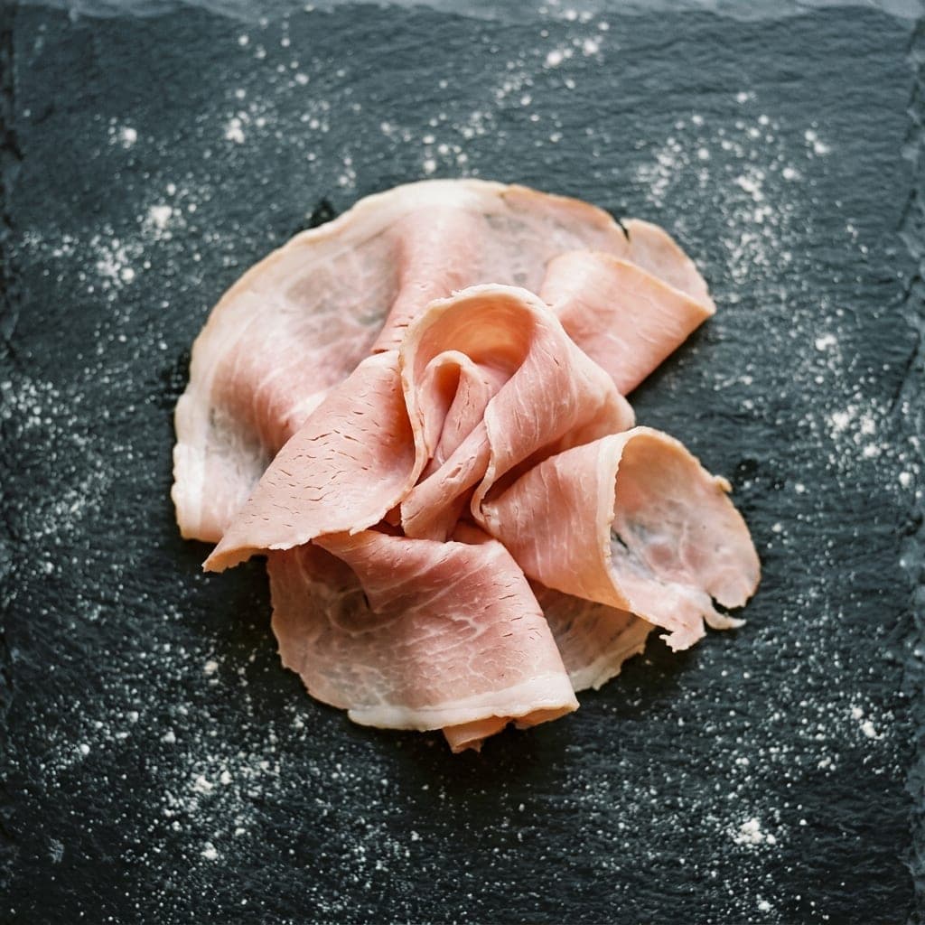 Thin slices of pale rosy prosciutto cotto torn into ribbons on dark slate