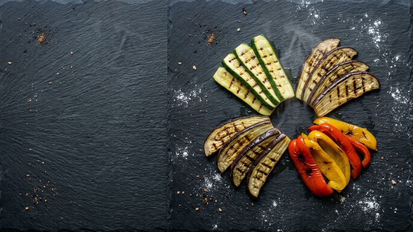 Grilled strips of zucchini, eggplant and red and yellow peppers with char marks, fanned out on dark slate